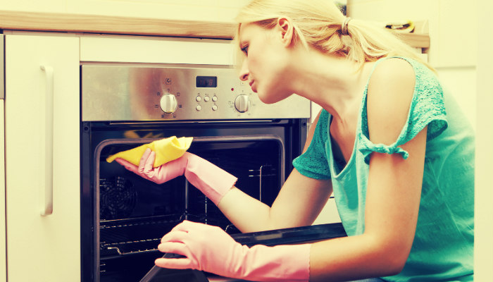 young woman wiping the oven with a rag