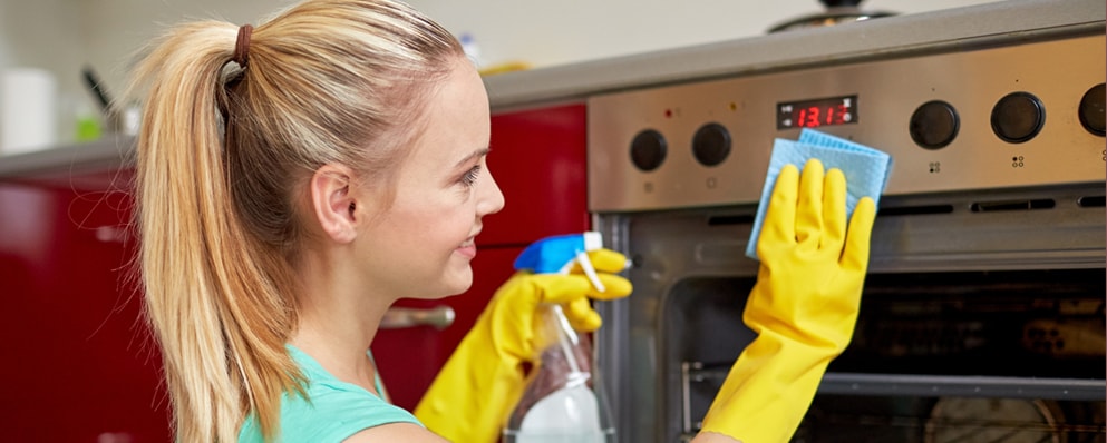 young girl wiping the metal surface of oven wearing protective gloves