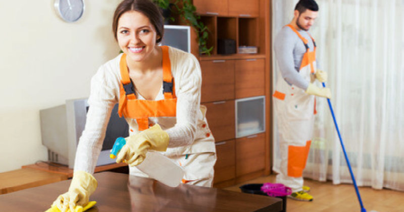 Young woman wiping wooden table and man mopping the floor