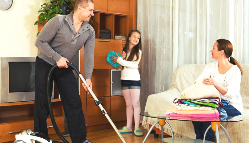 happy family of three dusting, vacuuming and arranging the room