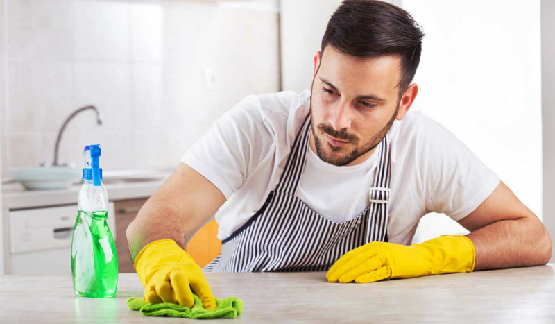 young man wearing apron wiping kitchen counter
