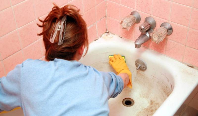 lady with yellow gloves scrubbing bathtub