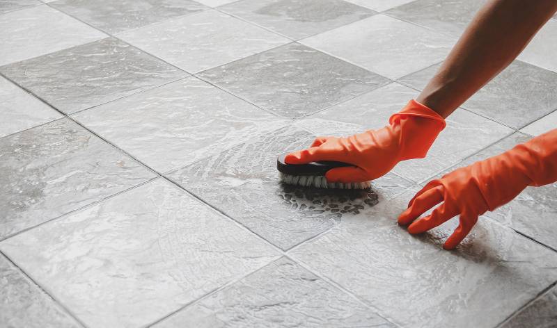 Hand of a woman in orange gloves scrubbing tile grout