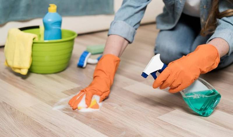 Woman in yellow gloves holding spray bottle in one hand and scrubber in second hand