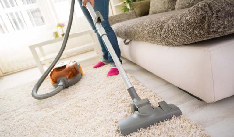 Woman using vacuum cleaner vacuuming carpet inside a living room.
