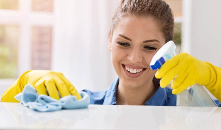 Woman in yellow gloves cleaning marble using a cloth and spray bottle in her hand.
