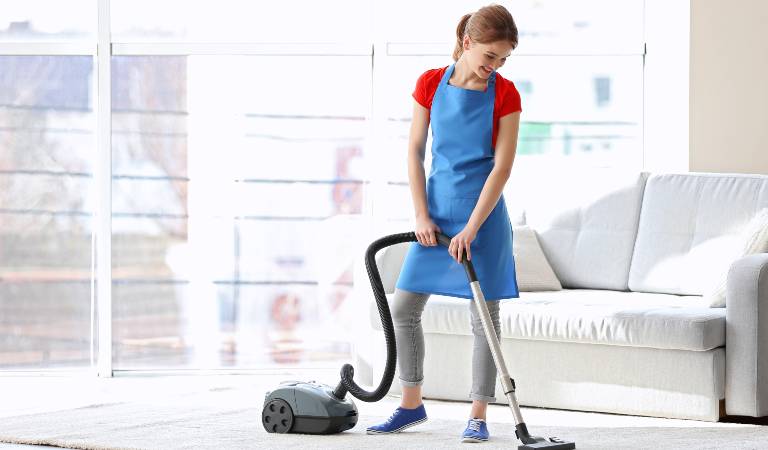 Woman in blue-red uniform using vacuum cleaner inside a living room.