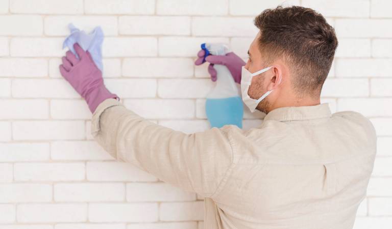 Man in purple glove and mark cleaning grout with a cloth