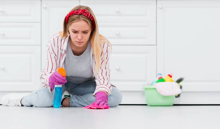 Woman in open shirt and pant holding a bottle in her hand cleaning floor