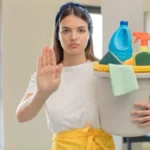 Woman in white top and yellow lower holding a cleaning basket showing a sign of stop with her hand.