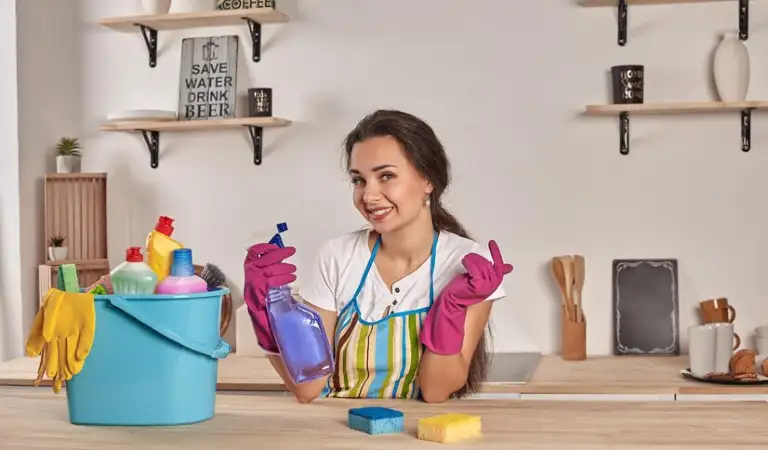 Lady in pink gloves holding a bottle with a blue cleaning basket on the table.