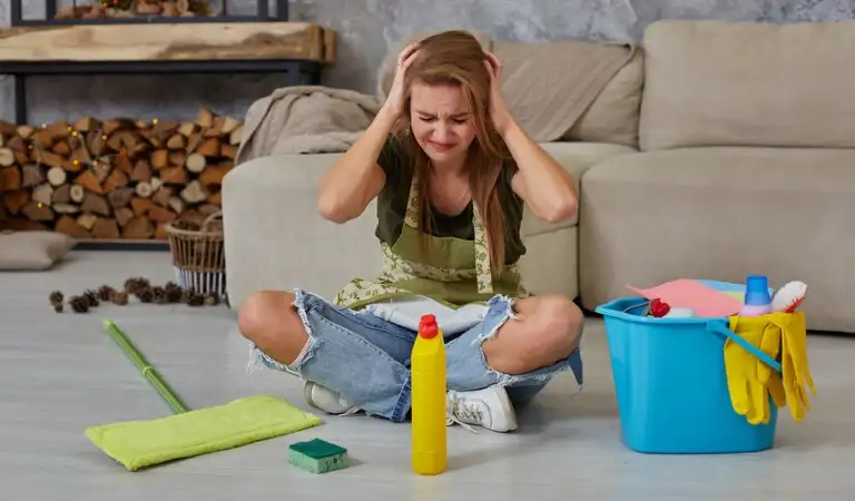 Woman housewife feel tired sitting on floor at living room after cleaning at home with blue bucket fulfilled with chemicals and facilities for tidying up