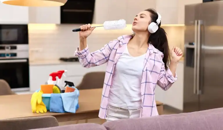 Lady listening music holding a duster and trying to sing.
