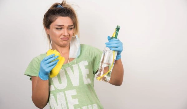 Young woman with facemask looks at spray on white wall