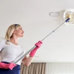 Maid woman holding mop pile, cleaning ceiling in living room