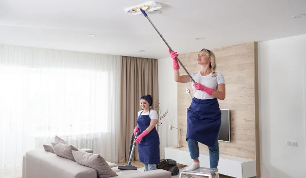 Woman standing on lsadder at home and cleaning ceiling with extended mop