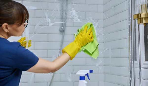 Woman cleaning bathroom washing glass in shower