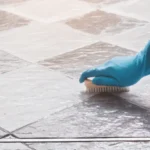 Hand of man wearing blue rubber gloves is used to convert scrub cleaning on the tile floor