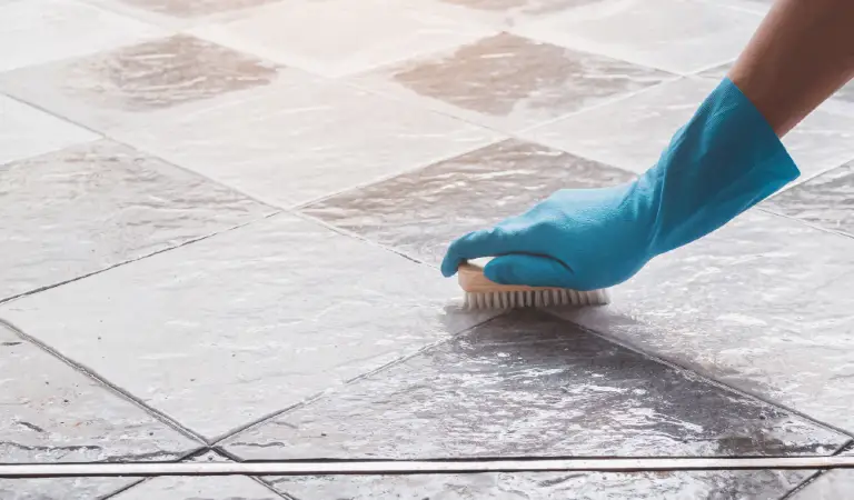 Hand of man wearing blue rubber gloves is used to convert scrub cleaning on the tile floor