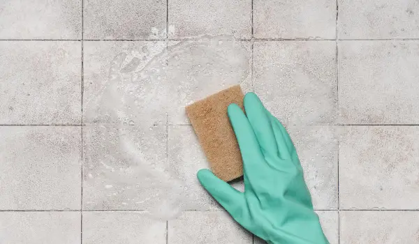 Woman's hand with cleaning tool on background of ceramic tiles