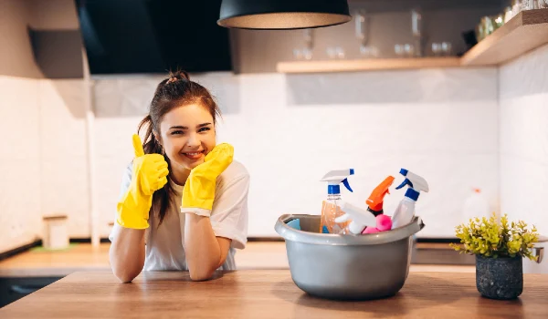 Young happy cute woman in yellow gloves is cleaning her kitchen at home with detergents