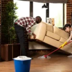 Young diverse couple doing housework and chores in living room black man lifting couch as girlfriend