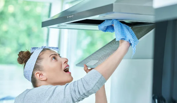 Young woman cleaning dirt in the kitchen range hood