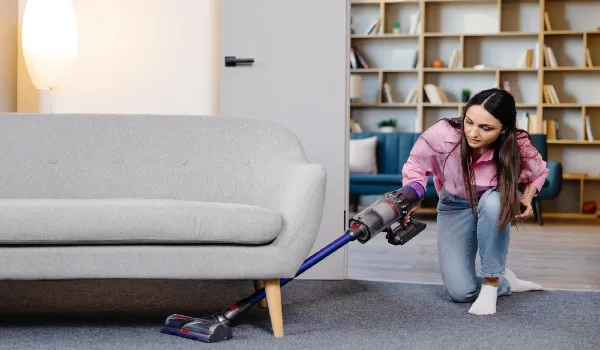 Young woman uses cordless vacuum cleaner to clean home carpet modern easy cleaning