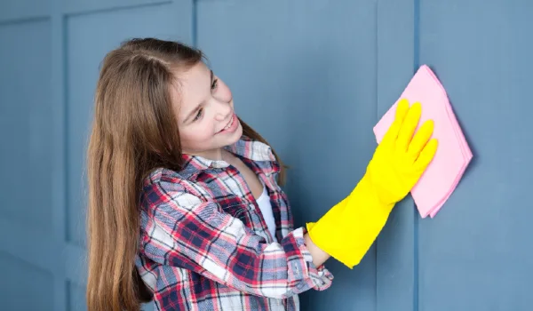 Household duties and child help. Little girl cleaning home walls